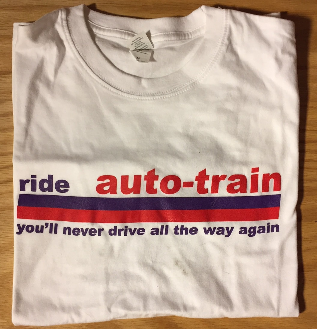 Photo of front of a folded T-shirt in white with auto-train logo on the chest.